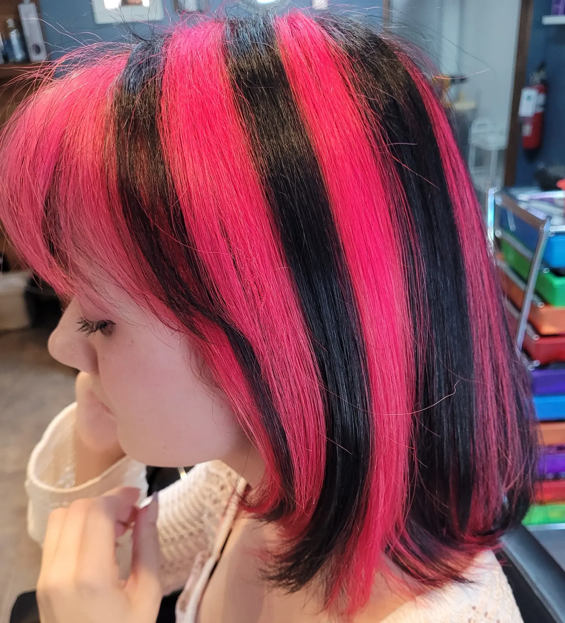 A blunt bob coloured in alternating hot-pink and black panels, seen from the side in the salon chair