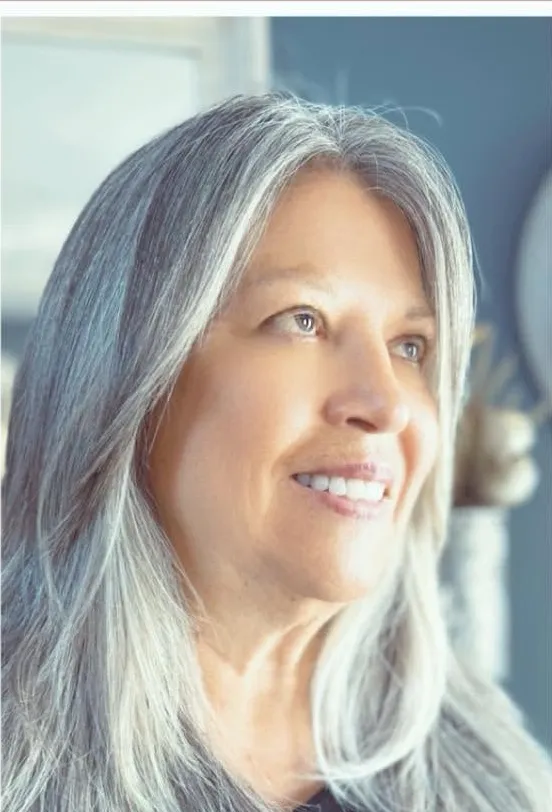 The same client after, silver hair cut into long layers, dimensional and blown out